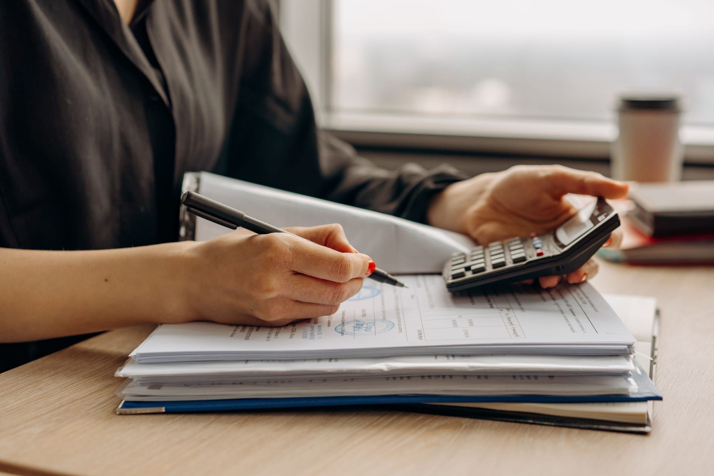 Close-up of hands checking a stack of financial documents with a pen and calculator