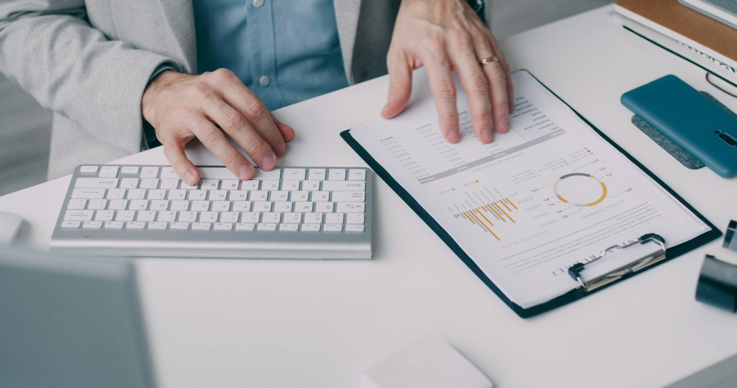 Hands typing on a keyboard beside a clipboard holding a printed financial report