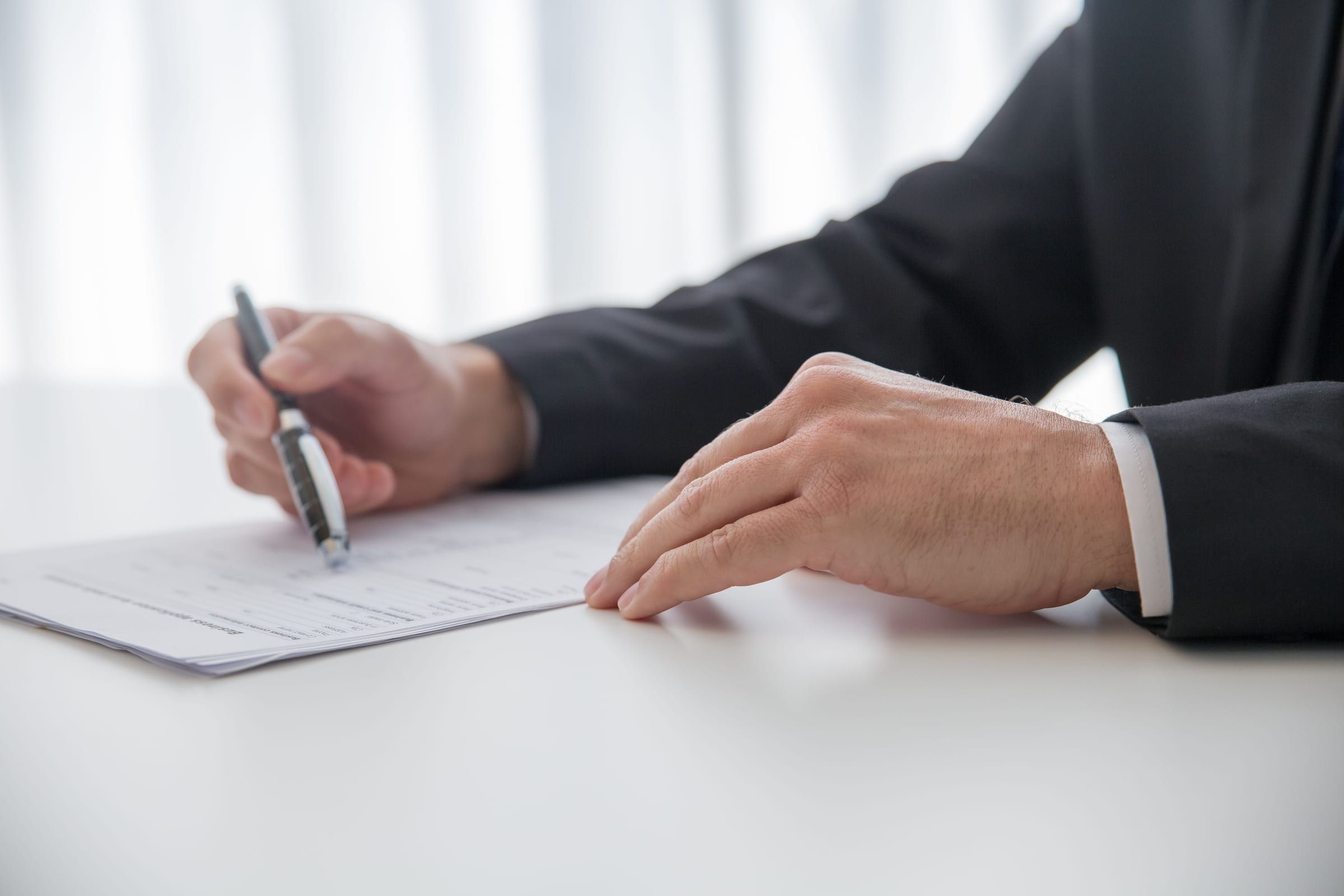 Close-up of a businessman in a dark suit signing a document at a white desk